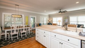 Une cuisine moderne avec des meubles blancs, un grand îlot central doté d’un évier et un coin repas avec une table et des chaises blanches.