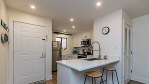 Cozinha moderna com armários brancos, uma ilha central com banquetas, micro-ondas e geladeira de aço inoxidável.