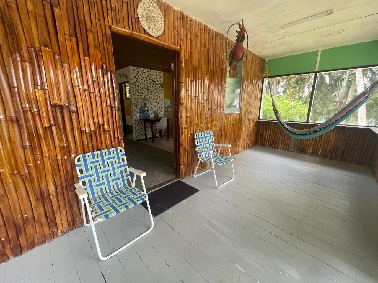Una habitación con paredes de bambú, dos sillas con estampado, una hamaca y vistas a la vegetación.