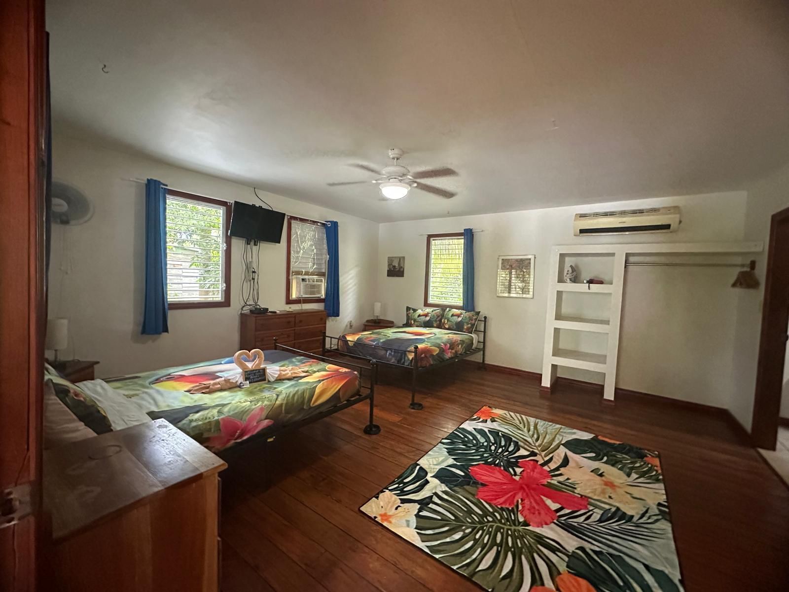 A bedroom with two beds, a ceiling fan, an air conditioning unit, and a wooden dresser.