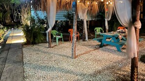 Un área de estar al aire libre con techo de paja, luces colgantes y un camino de grava.