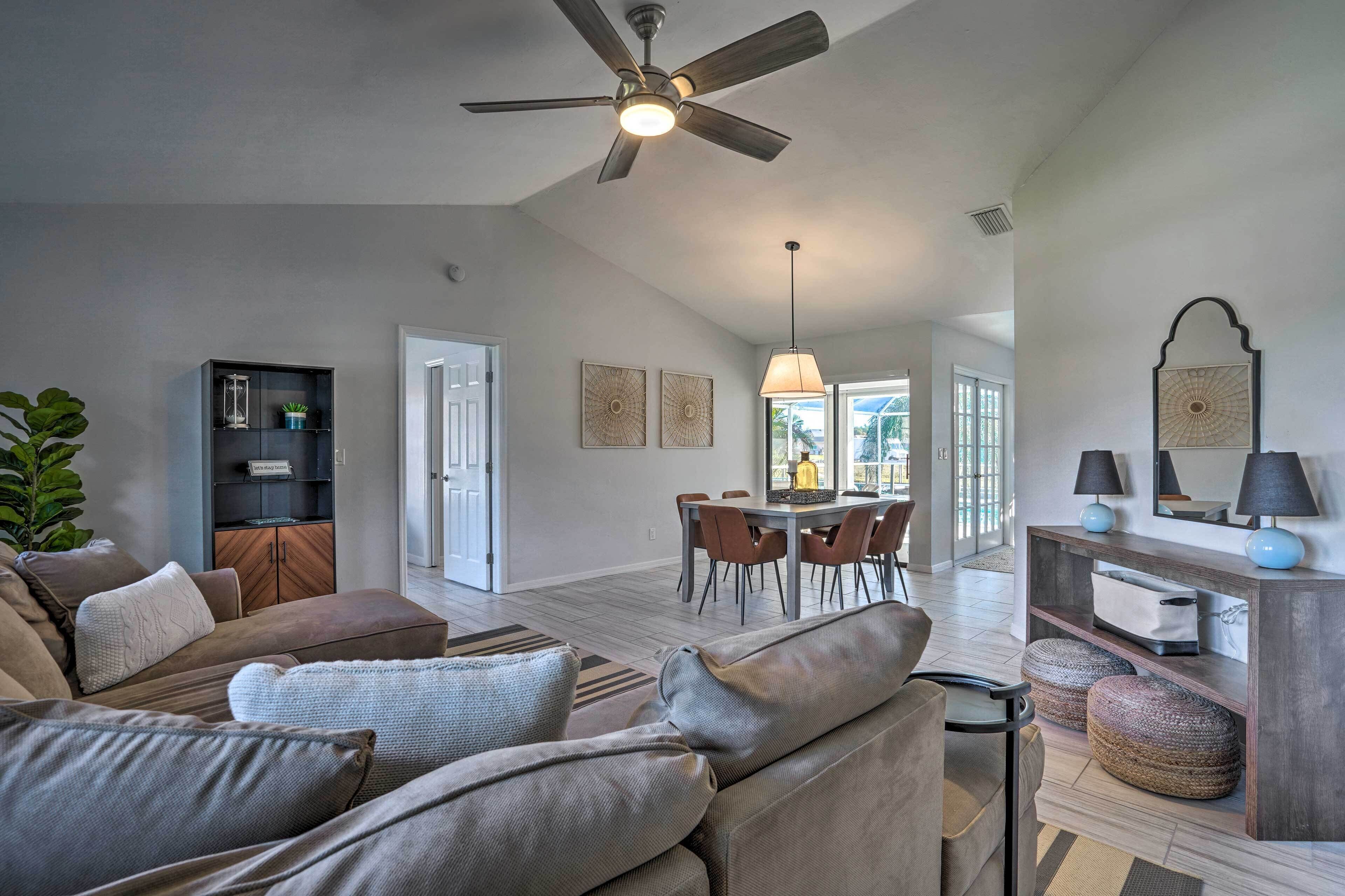 A spacious living room with a ceiling fan, a dining area with a table and chairs, and a modern console table with lamps.