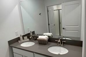 A modern bathroom with two sinks, a large mirror, and a door. - Storey Lake home close to Disney and other parks (KISSIMMEE FL)