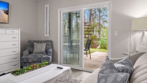 A living room with a sofa, a coffee table, a TV, and a sliding glass door leading to an outdoor area with a patio chair and a garden. - Spacious 2 bedroom condo (North Charleston)