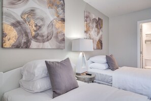 A hotel room with two beds, a bedside table with a lamp, and abstract wall art.