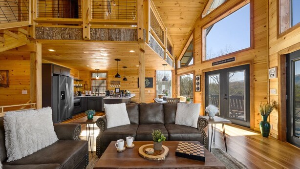 Eine geräumige Hütte mit hohen Decken, einem gemütlichen Wohnbereich mit Sofa und Couchtisch, einer Küche und großen Fenstern mit Blick ins Freie.