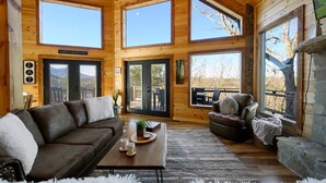 Ein gemütliches Blockhaus-Interieur mit einer großen Holzbalkendecke, mehreren Fenstern, einem Kamin und einer komfortablen Sitzecke.
