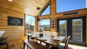 A wooden interior with a dining table set for four, large windows, and a sign reading "Good food - Good friends - Good times". - BeautifulMtViewResortIndoorPool/Spa2CabinsPFNearIsland/Strip Game Room 16-18ppl (Pigeon Forge)