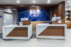 Un mostrador de recepción de hotel con un diseño moderno, con dos mostradores con detalles de madera y un fondo de pared azul con motivos geométricos.