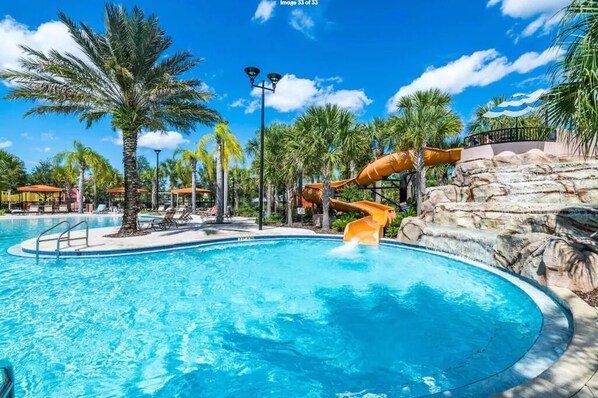 Relax by the pool surrounded by palm trees and a rocky outcrop, with a water slide and splash pool nearby.