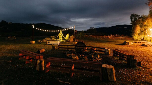A campsite with a wooden bench, a fire pit, and a tent under string lights. - A Little Blue Farmhouse:TemeculaWine Country Farm (Sage)