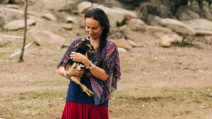 A person holding a goat in an outdoor setting with rocks and sparse vegetation. - A Little Blue Farmhouse:TemeculaWine Country Farm (Sage)