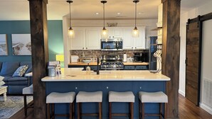 Een moderne keuken met een centraal eiland, barstoelen, hanglampen en uitzicht op de woonkamer.