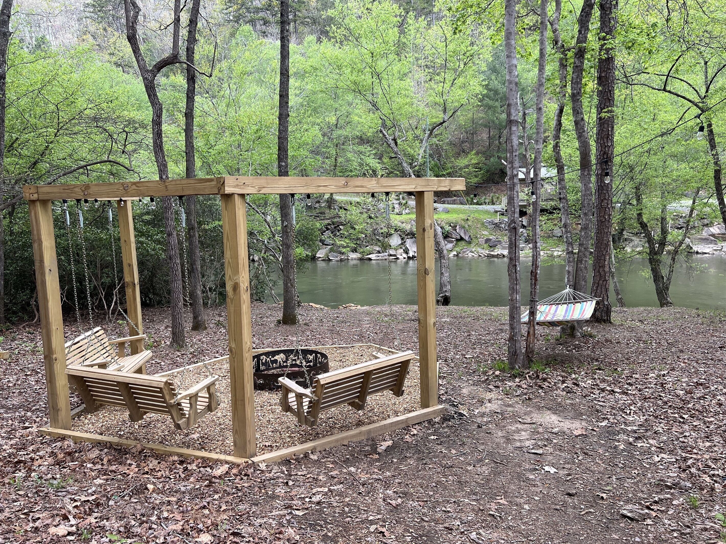 A wooden swing set with benches in a wooded area near a river.