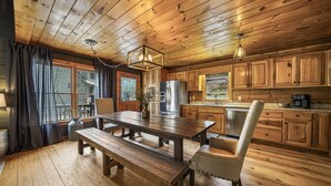 Ein Holzblockhaus-Interieur mit Esstisch, Bänken, einem Stuhl, einem Kühlschrank und Holzschränken.