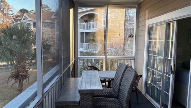 Een balkon met een tafel en stoelen, grote ramen en een plafondventilator.