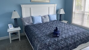 Een slaapkamer met een bed, twee nachtkastjes, een lamp, een lijst met een afbeelding en een raam met jaloezieën.