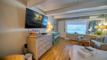 Une chambre d’hôtel équipée d’une télévision, d’un bureau avec une lampe, d’un fauteuil en osier, d’un lit avec des serviettes et d’une fenêtre avec des stores.