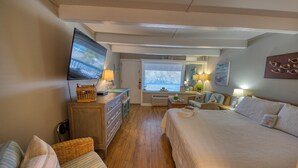 Une chambre à coucher comprenant un lit, une télévision, une commode, une chaise, une fenêtre avec des stores et un miroir.