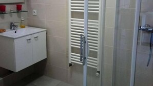 Uma casa de banho com chuveiro em cabine de vidro, uma pia branca com espelho em cima e um porta-toalhas com toalhas brancas.