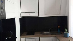 Una cucina compatta con mobili bianchi, una schiena di cucina nera, una lavastoviglie integrata e un piccolo oblò con una pianta.