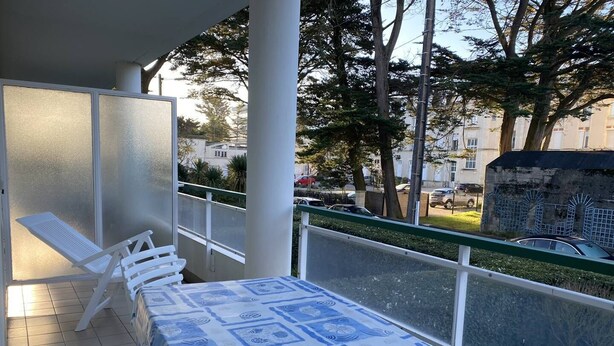 A balcony with a table and chairs, overlooking a street with parked cars and buildings. - Location de Vacances - Pornichet-2 Pièces-005-60282 (PORNICHET)