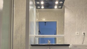A compact bathroom with a built-in washing machine, a mirror with lights, and a shower enclosure. - Location de Vacances - Pornichet-2 Pièces-005-60282 (PORNICHET)