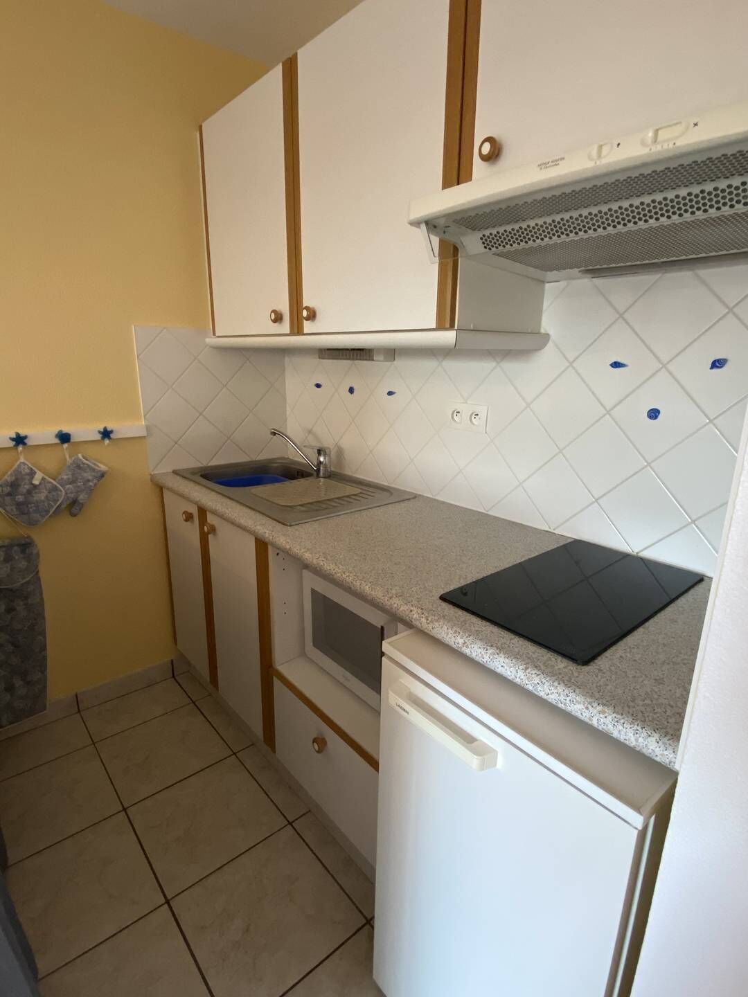 Une cuisine de taille réduite avec des meubles blancs, un four à micro-ondes, un évier et une planche à découper noire posée sur le plan de travail.