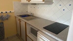 A compact kitchen with white cabinets, a microwave, a sink, and a black cutting board on the countertop. - Location de Vacances - Pornichet-2 Pièces-005-60282 (PORNICHET)