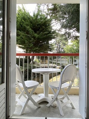 Un balcon avec une table blanche et deux chaises blanches, entouré d’une rambarde en métal.