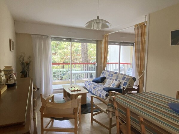 Une pièce confortable avec un canapé, une petite table et une chaise. Il y a un balcon avec une balustrade et une vue sur les arbres.