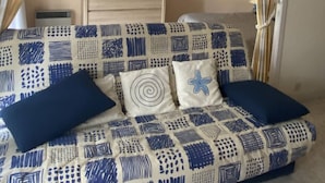 Ein Zimmer mit einer gepolsterten Couch, einem kleinen Tisch mit Bilderrahmen und Vorhängen.