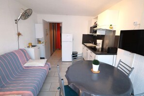 Um espaço de estar compacto com sofá, mesa de jantar, cozinha compacta e televisão.