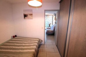 Quarto com cama, um quadro, janela com cortinas e corredor que dá para outro cômodo.