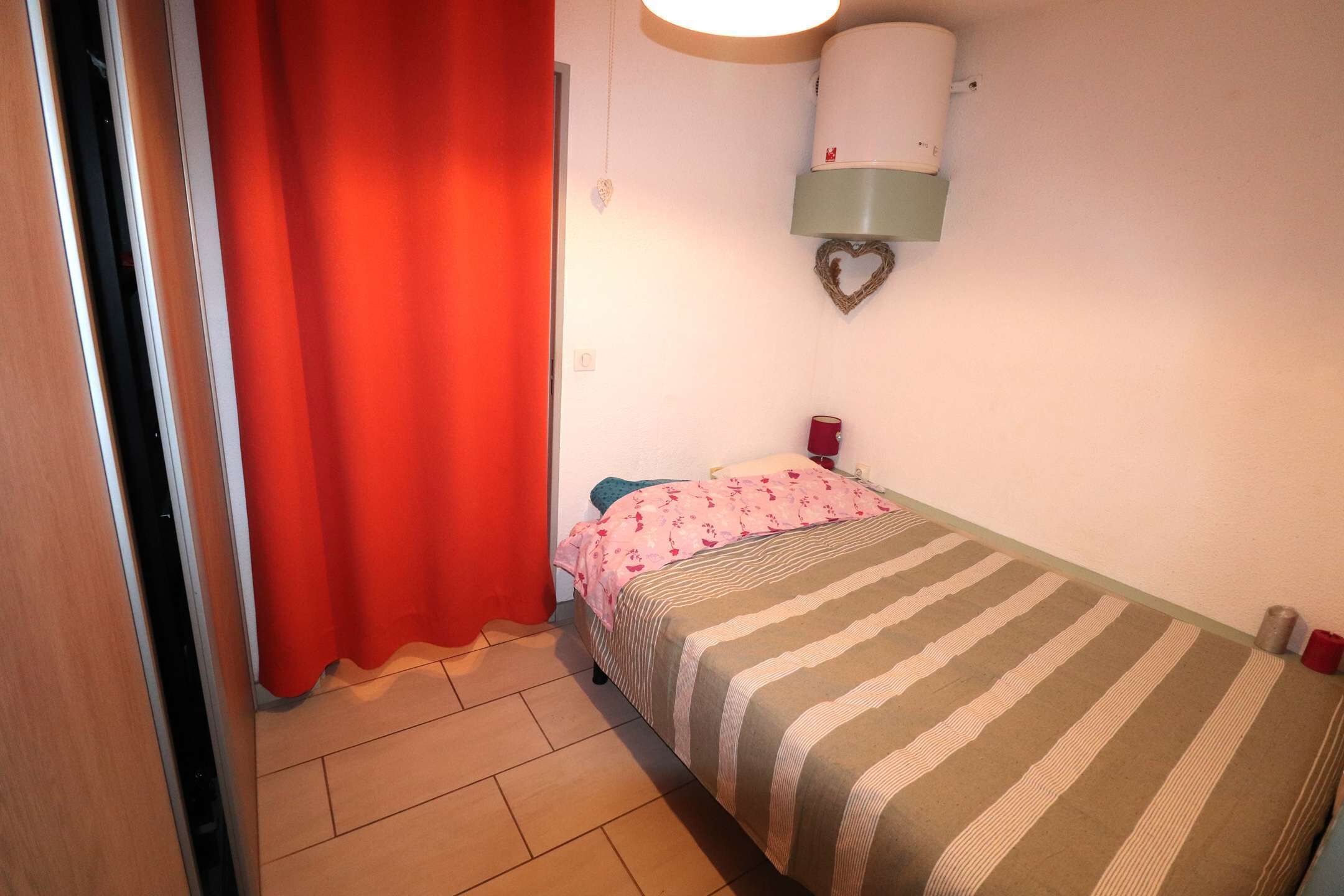 Ein Schlafzimmer mit einem Bett, einem roten Vorhang, einem Wandheizkörper und einer herzförmigen Dekoration.