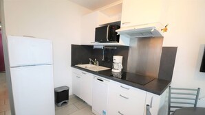 Una cocina compacta con un refrigerador blanco, un lavamanos, una cafetera y un microondas.