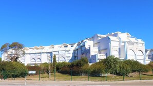 Un edificio grande y blanco con varios balcones y ventanas arqueadas, rodeado de follaje y un cielo azul despejado.