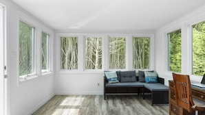 Una habitación con un banco empotrado, un escritorio y ventanas amplias con vistas a árboles.