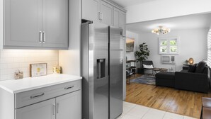 Una cocina moderna con armarios grises, un refrigerador de acero inoxidable y una zona de comedor con un sofá negro y una mesita.