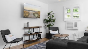 Una sala de estar moderna con un televisor de pantalla plana, una planta grande, un sofá acogedor, una mesita de madera y una pequeña mesa redonda.