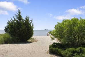 A sandy beach path leading to a body of water, surrounded by dense green foliage and a clear sky. - Beautiful remodeled 2 bedroom home — 5 min from the beach! 20 percent for week  (east quogue)