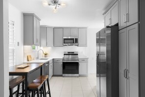 A modern kitchen with grey cabinets, stainless steel appliances, a wooden bar counter, and bar stools. - Beautiful remodeled 2 bedroom home — 5 min from the beach! 20 percent for week  (east quogue)