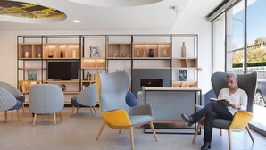 A modern lounge area with seating, a fireplace, and a large window offering a view. - Studio Confortable avec Wi-Fi et Climatisation (Toulouse)