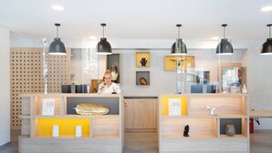 Zona de recepción con un escritorio de madera, una recepcionista y una barra con diversos objetos.