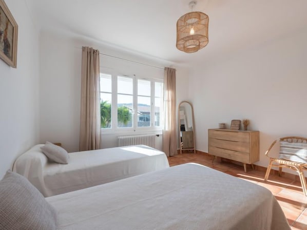 A bedroom with two beds, a dresser, a chair, a mirror, and a window with curtains.