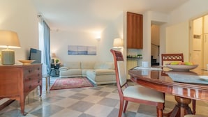 A living room with a sofa, a dining table with chairs, a wooden cabinet, and a television.