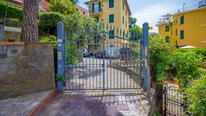 A gated entrance to a residential area with a stone wall, a metal gate, and a yellow building in the background.