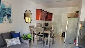 Un salon moderne avec un canapé gris, une table à manger avec des chaises, un coin cuisine doté de meubles en bois et un réfrigérateur.