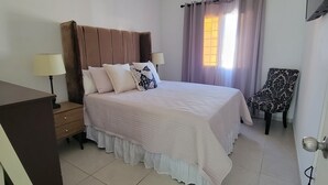 Une chambre bien rangée, avec un lit, des lampes de chevet, une chaise et une fenêtre avec des rideaux.