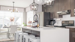 Et moderne køkken med en central ø, barstole, rustfrie stålapparater og hængende lamper.